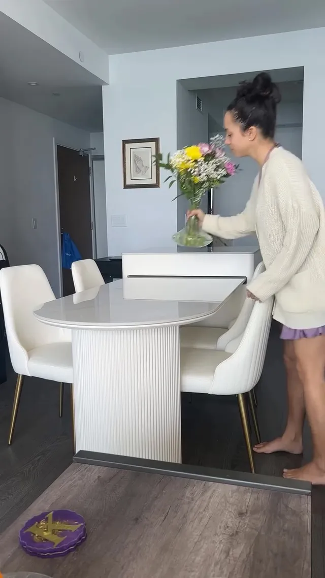 Kiana Madeira standing barefoot in a cardigan and shorts beside flowers.