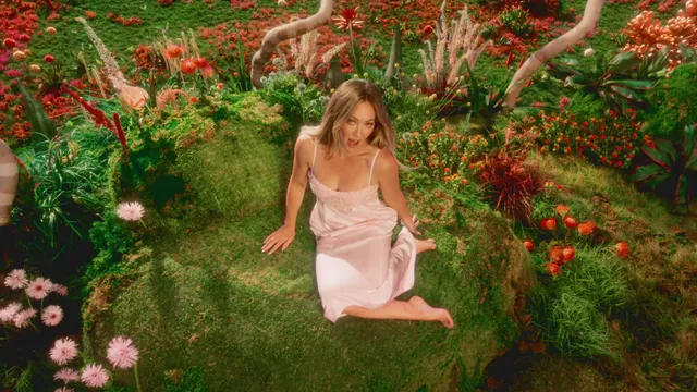 Hilary Duff sitting barefoot amid flowers in a colorful studio scene.