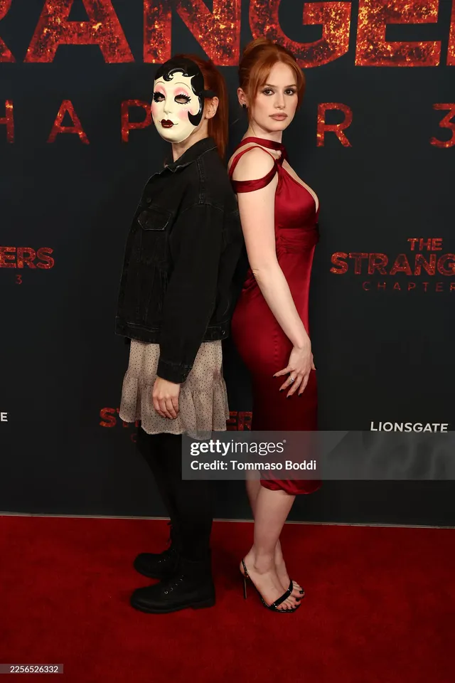 Madelaine Petsch posing beside a guest in a red dress and heels.