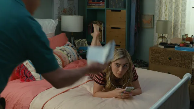 Meg Donnelly reclining barefoot on a bed in a striped top.
