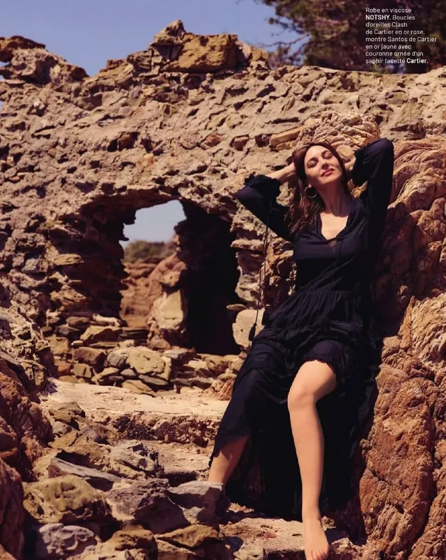 Monica Bellucci leaning against stone ruins in a black dress.