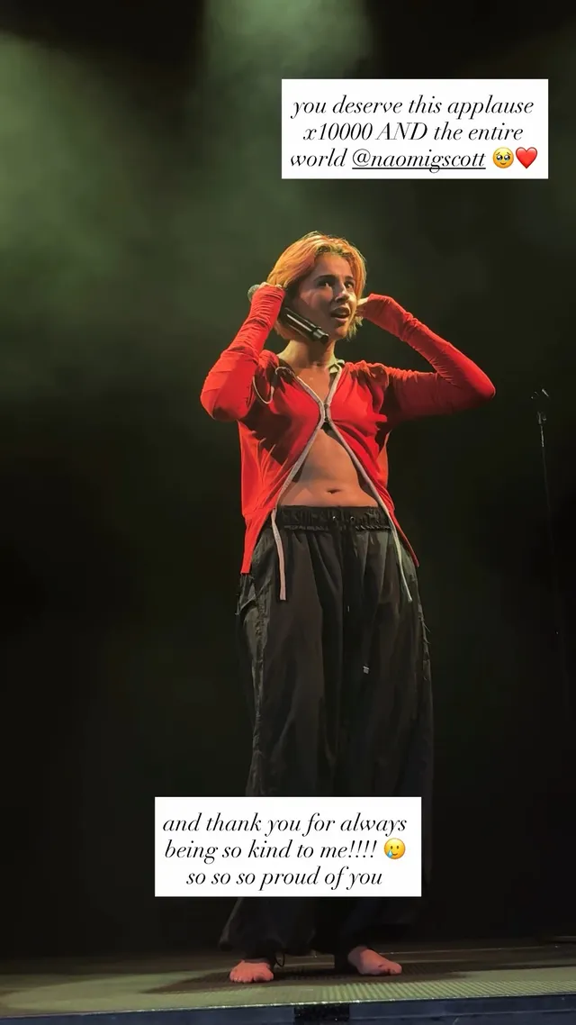 Naomi Scott singing barefoot onstage in a red jacket.
