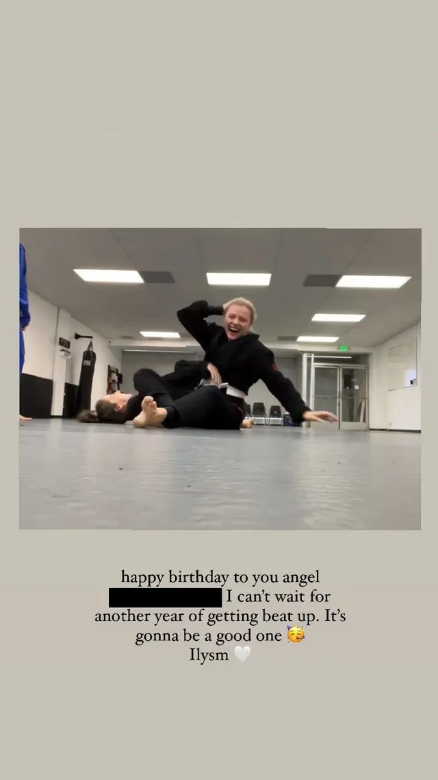 Chloë Grace Moretz sitting barefoot on a gym floor beside a training partner.