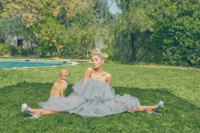 Ariana Grande seated outdoors in a flowing pale blue gown and pointed heels.