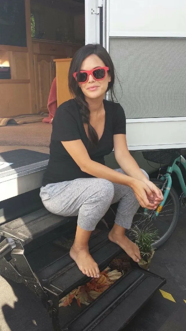Rachel Bilson sitting on an outdoor bench wearing sunglasses.