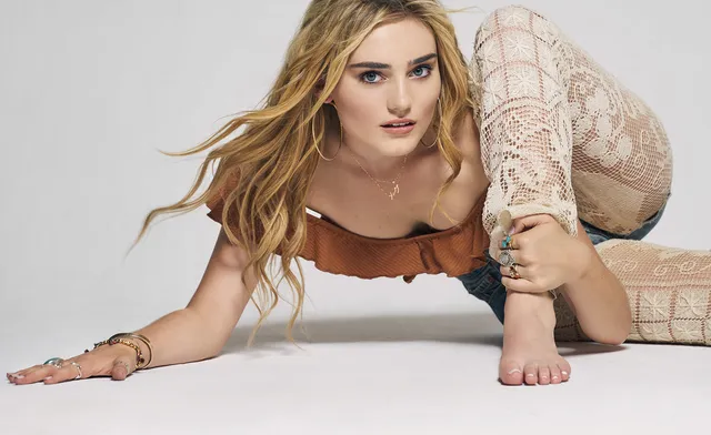 Meg Donnelly crouching barefoot on a studio floor in a patterned outfit.