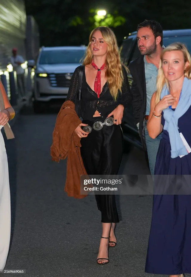 Grace Van Patten standing with guests in a black outfit and strappy heels.