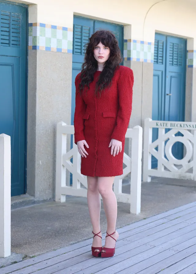 Sophie Thatcher posing in a red suit and red platform heels.