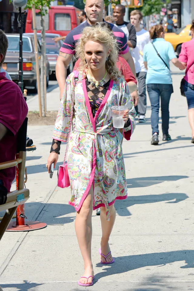 AnnaSophia Robb walking outdoors in a patterned robe and flip-flops.