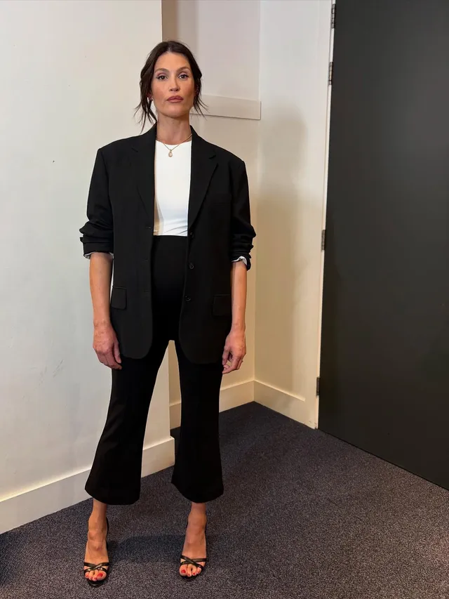 Gemma Arterton standing in a black suit and sandals.
