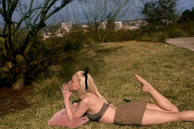 Anya Taylor-Joy relaxing barefoot on the grass in a dark swimsuit.