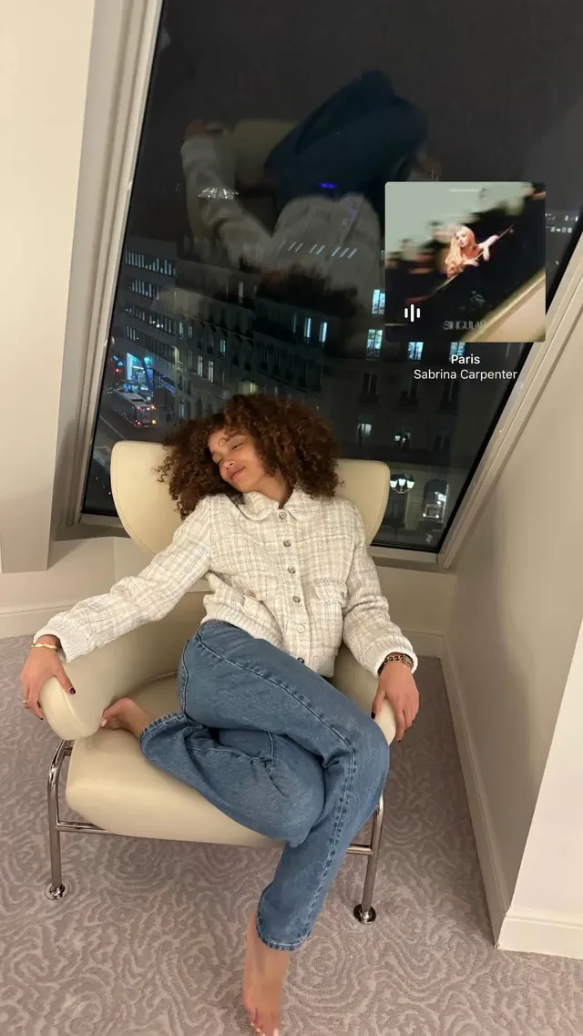 Whitney Peak sitting barefoot in a chair wearing jeans and a white blouse.