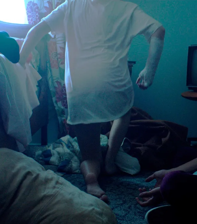 Maika Monroe standing barefoot beside a bed in a scene.