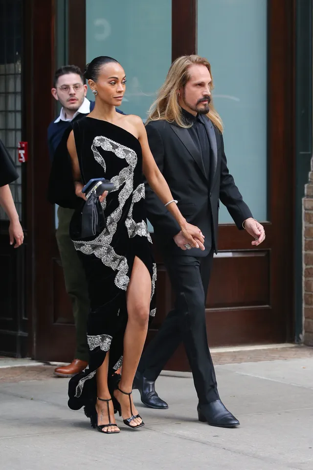Zoe Saldaña walking beside a guest in a one shoulder gown.