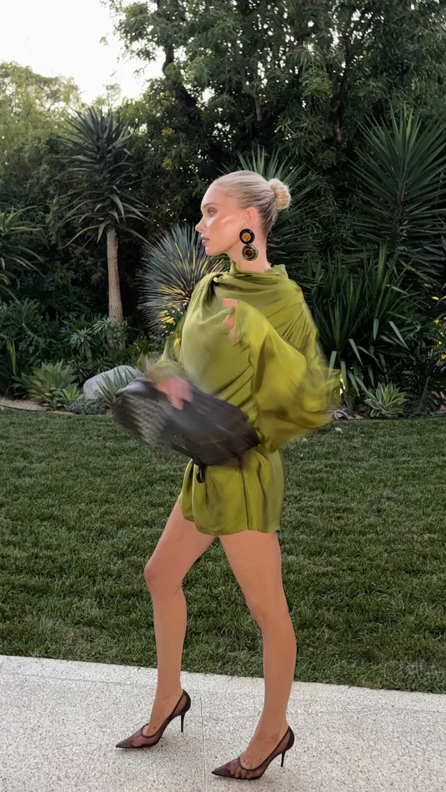 Elsa Hosk wearing patterned heels with a green outfit on a garden path.
