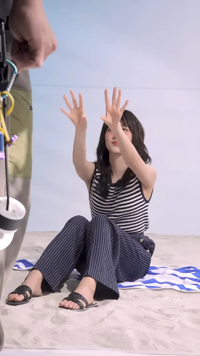 Jisoo sitting on a towel in black flat slides during a striped-top fashion shoot.