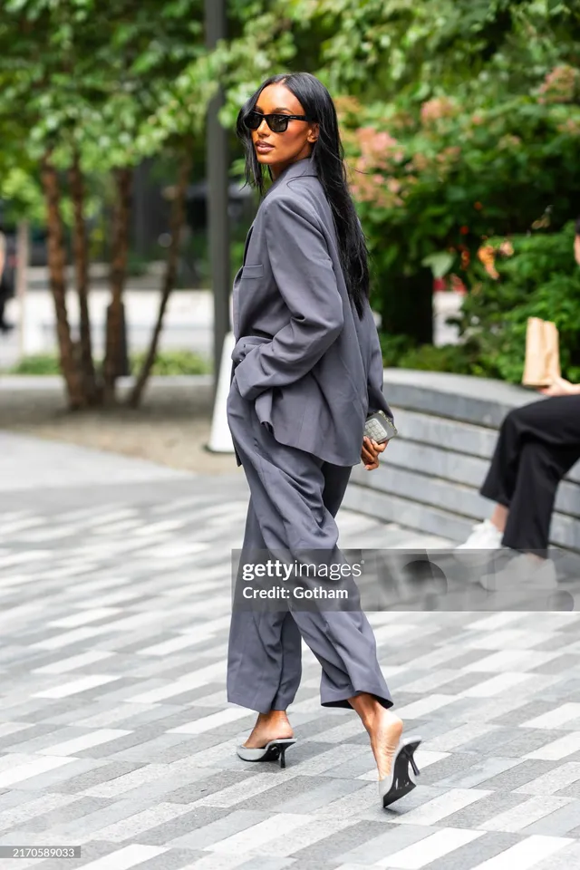 Jasmine Tookes walking in pointed black heels and a grey suit.