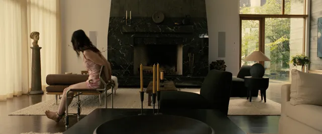 Sophie Thatcher leaning forward barefoot on a chair in a film scene.