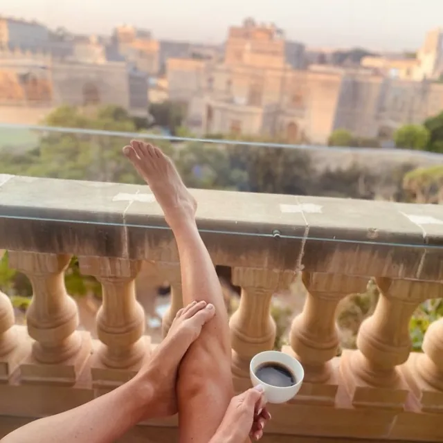 Alice Eve relaxing on a balcony with one leg raised.