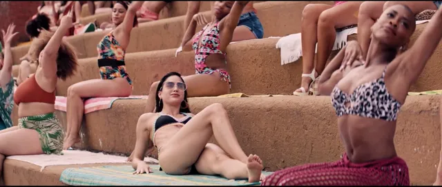Melissa Barrera sitting barefoot on tiered seating among other performers.