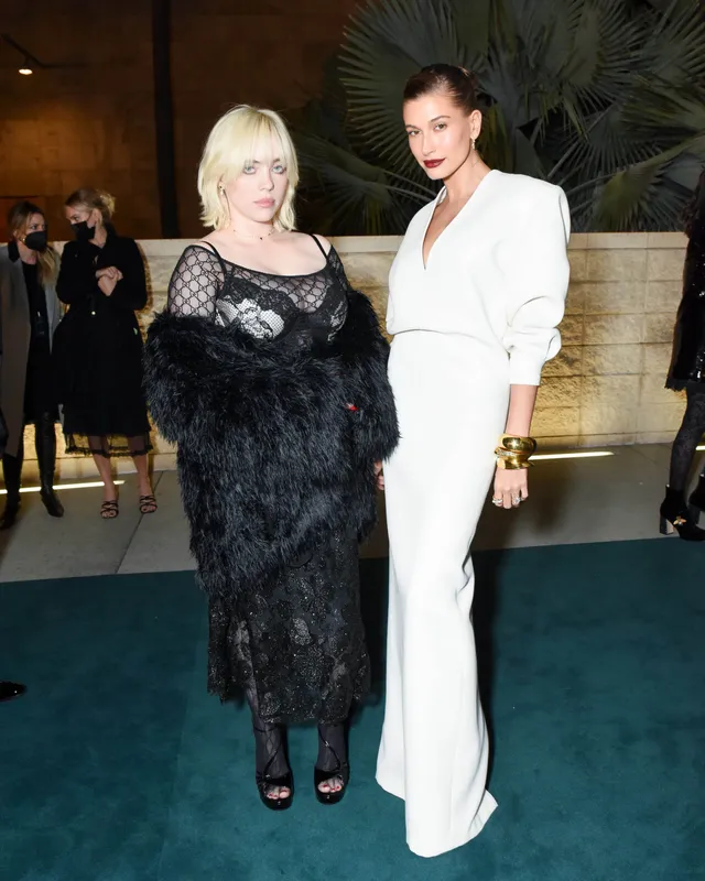 Billie Eilish posing beside another guest in a lace dress and dark heels.