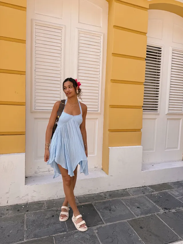 Madison Bailey wearing a pale blue dress and white flat sandals outside a building.