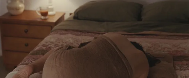 Elizabeth Olsen lying on a bed in a dimly lit film scene.
