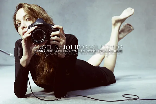Angelina Jolie lying on the floor holding a camera with her feet raised.