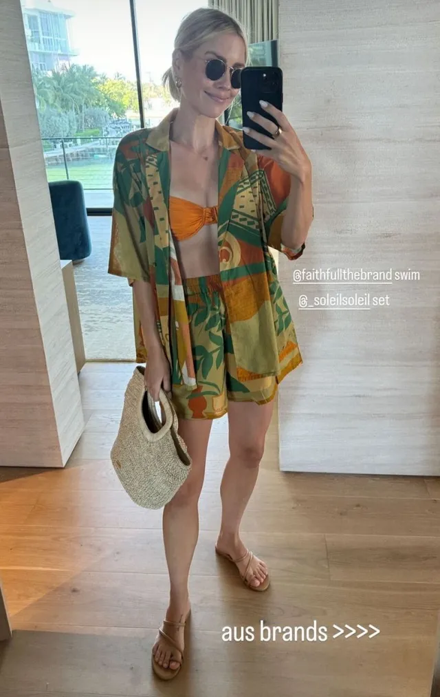 Claire Holt taking a mirror portrait in a colorful outfit and flat sandals.