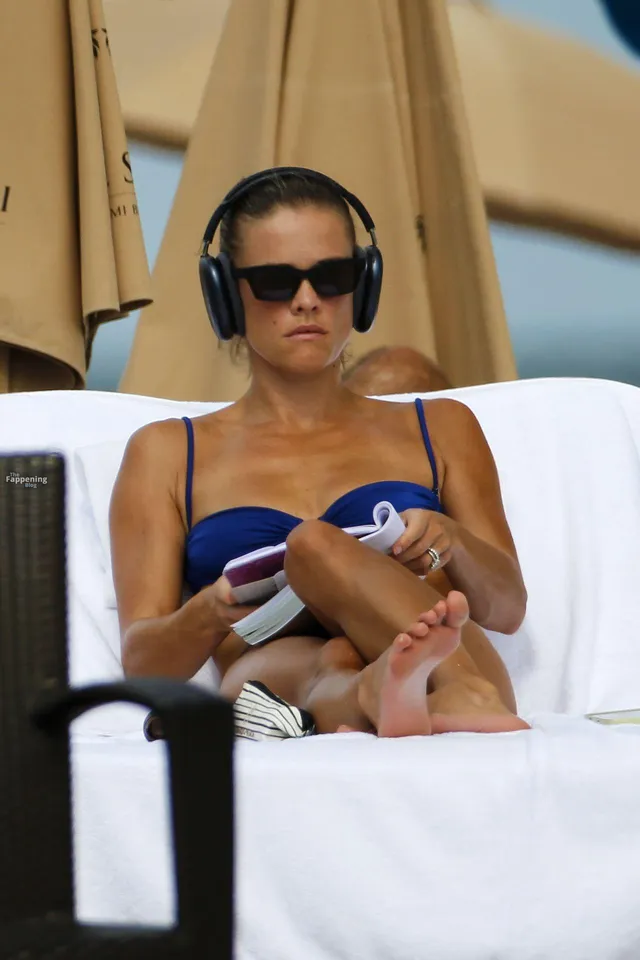 Nina Agdal sitting on a beach lounger with her bare feet crossed.