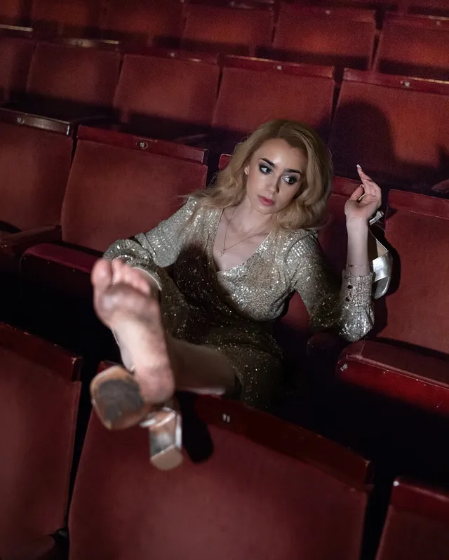 Lily Collins sitting in theater seats with a bare sole raised.
