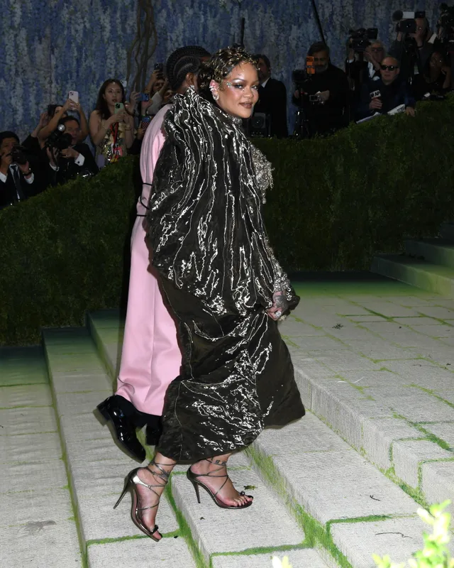 Rihanna walking outside at night in a shimmering coat and heels.