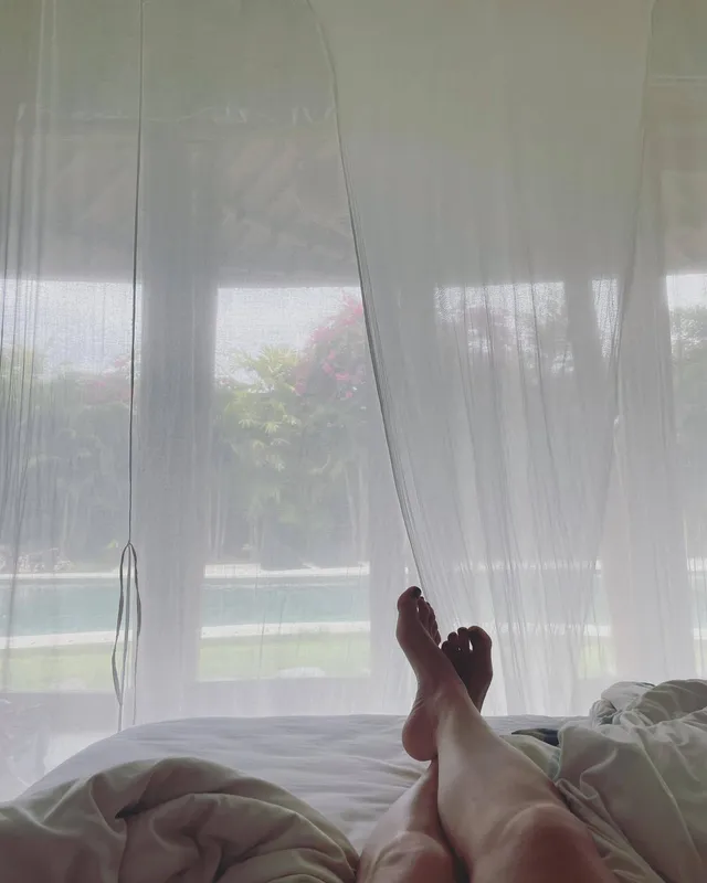 Tove Lo resting crossed bare feet on a bed beside a window.