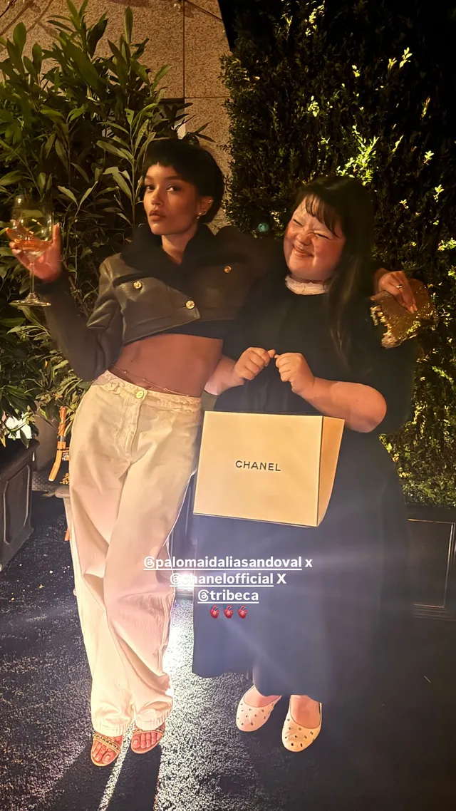 Whitney Peak posing with a friend in white trousers and heels outdoors.