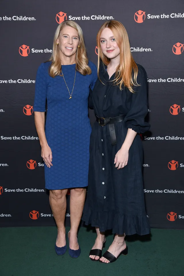 Dakota Fanning posing in a dark dress and sandals beside another woman at an event.