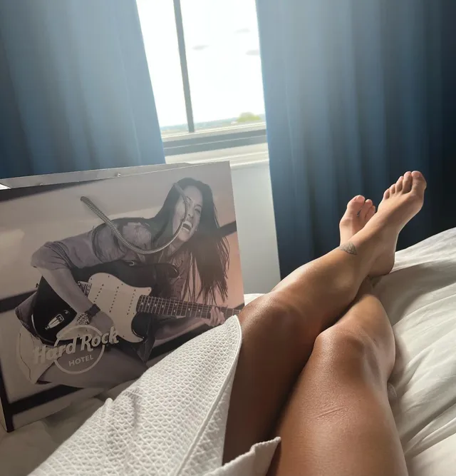 Alisha Lehmann resting her bare feet on a bed beside a shopping bag.