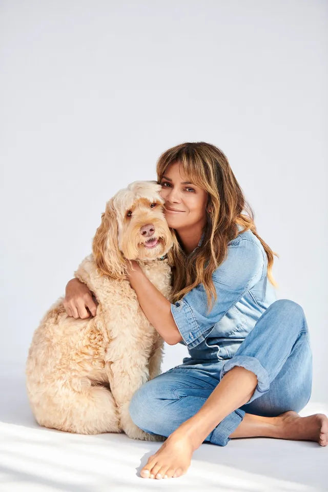 Halle Berry sitting barefoot in a denim outfit with a dog.