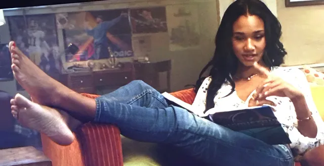 Greta Onieogou reclining barefoot in jeans while reading indoors.