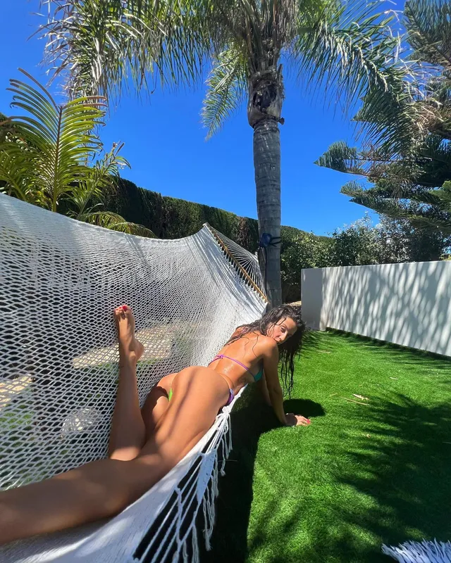 María Pedraza reclining barefoot in an outdoor hammock beneath palm trees.
