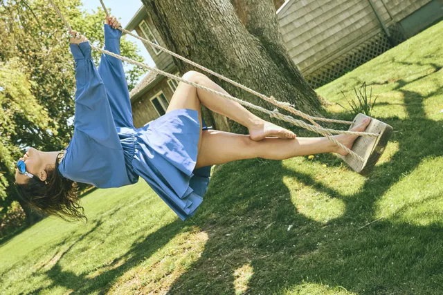 Bailee Madison sitting on a swing in a blue dress and pale heels.