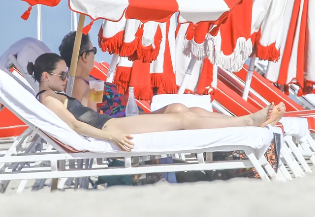 Daisy Ridley relaxing on a lounger under striped umbrellas.