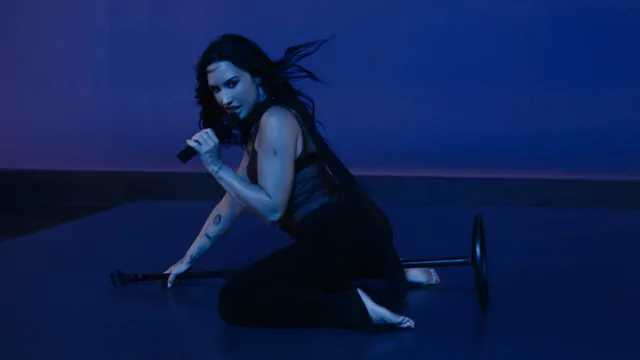 Demi Lovato performing barefoot in a blue-lit studio setting.