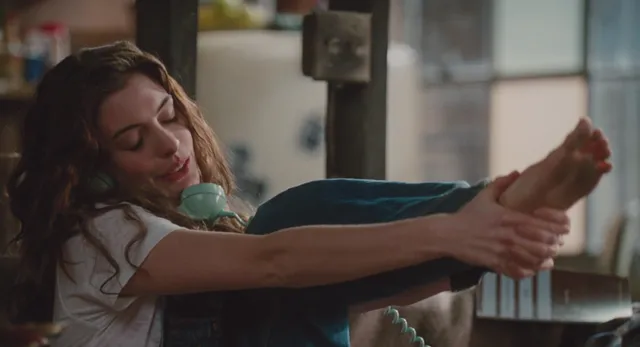 Anne Hathaway stretching while holding a raised bare foot.