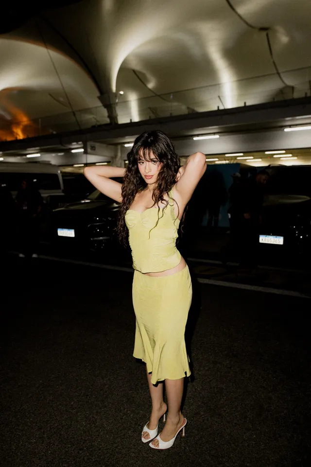 Camila Cabello posing in a yellow dress and white heels.