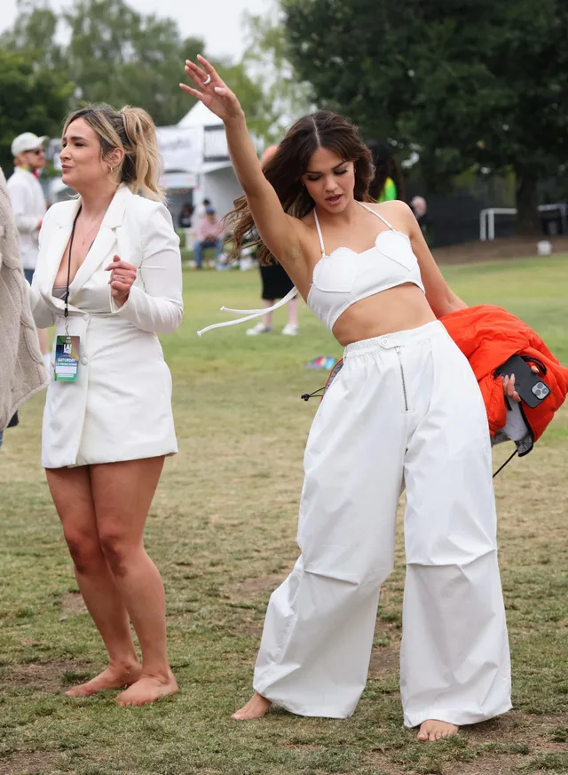 Maia Mitchell standing barefoot on grass in white trousers.