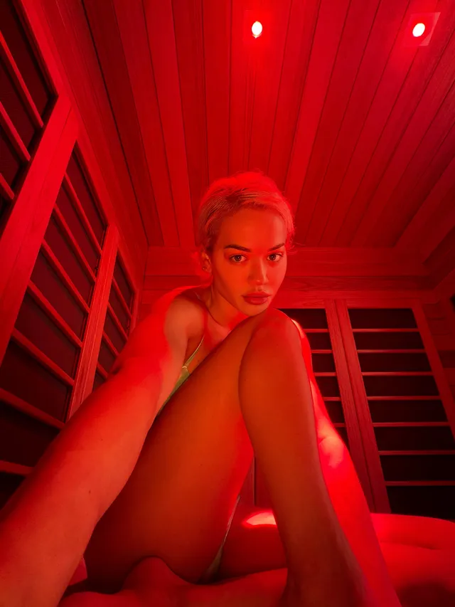 Rita Ora sitting under red sauna lighting.