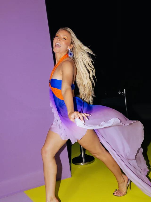 Zara Larsson posing in a flowing purple outfit and metallic heels.
