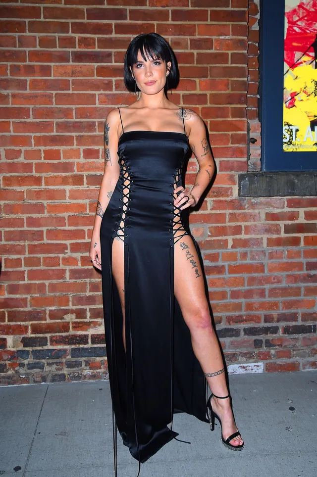 Halsey a black dress and heels beside a brick wall.