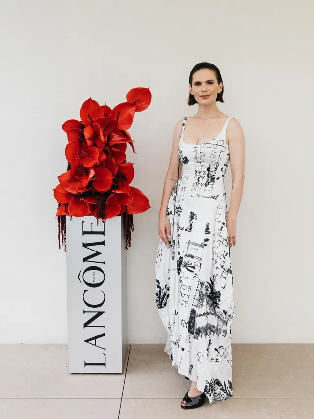 Hayley Atwell posing beside a floral display in a printed dress.