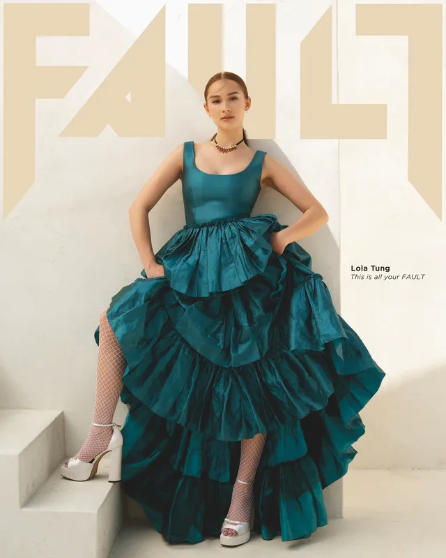 Lola Tung posing in a tiered teal dress, light socks and white heels.